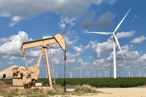 An oil derrick next to a wind farm